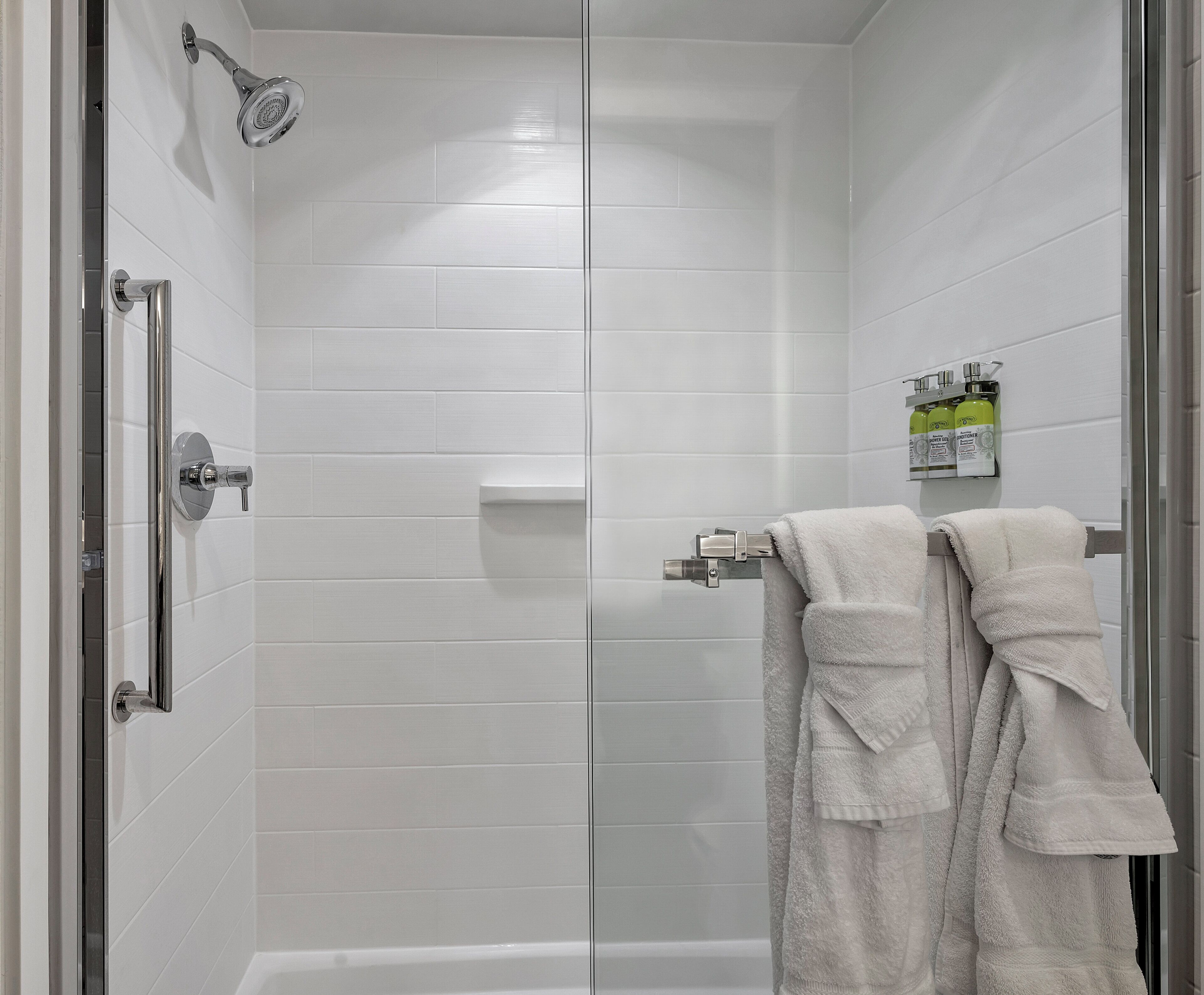 Een moderne douche met glazen deur, een handdouche en een handdoekhouder met twee handdoeken.