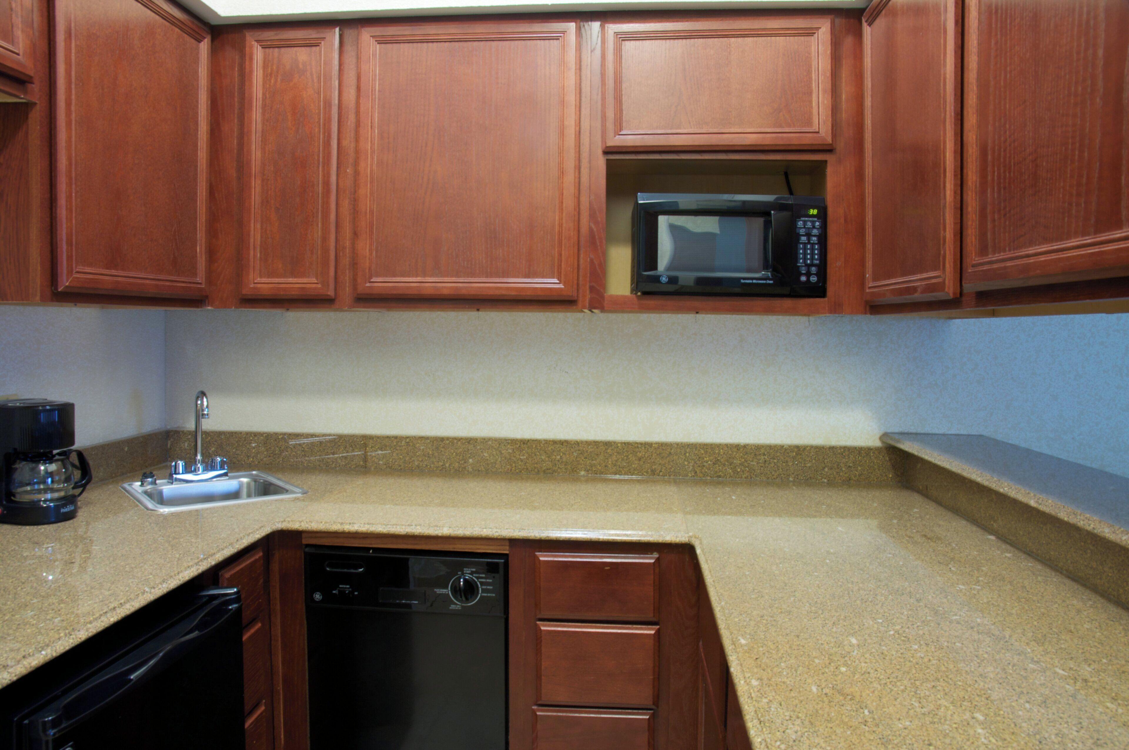 A kitchen with wooden cabinets, a built-in microwave, a coffee maker, and a dishwasher.