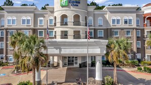 Un hotel Holiday Inn Express & Suites con una torre central, varios balcones y una entrada ajardinada.