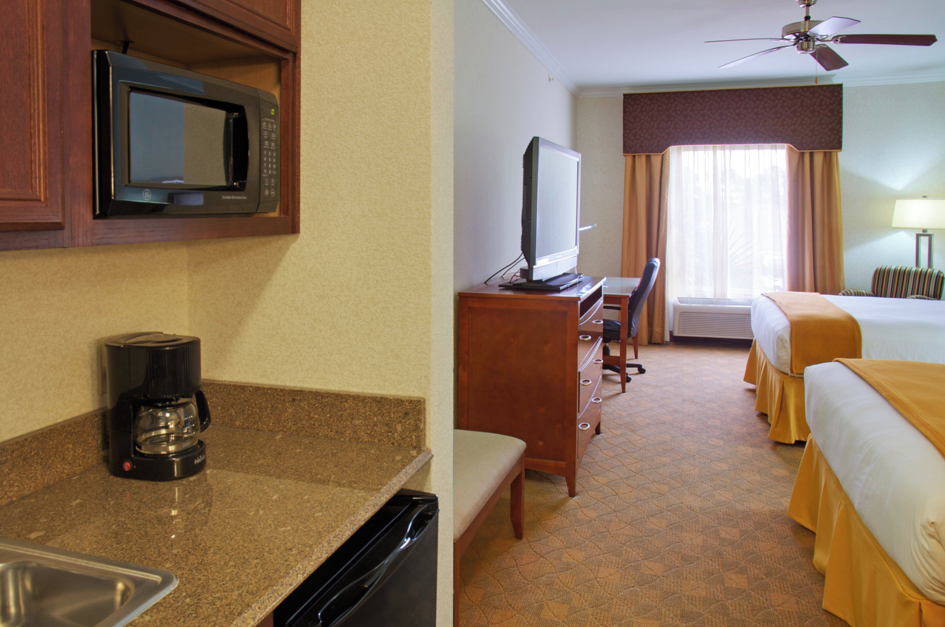 A hotel room with a kitchenette, a bed, a television, and a ceiling fan.