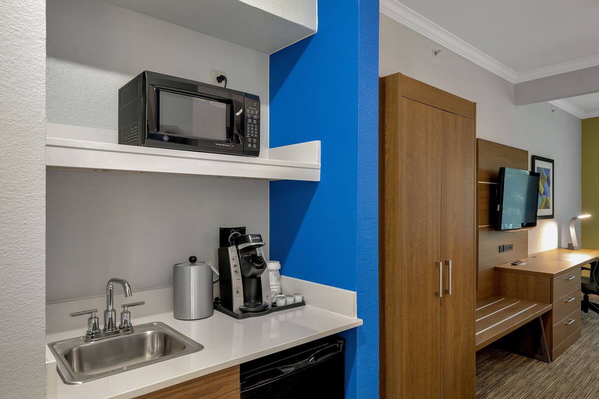 A compact kitchenette with a microwave, coffee maker, and sink.