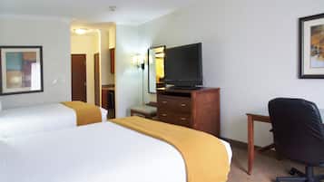 A hotel room with two beds, a television on a wooden dresser, a desk with a chair, and a ceiling fan.