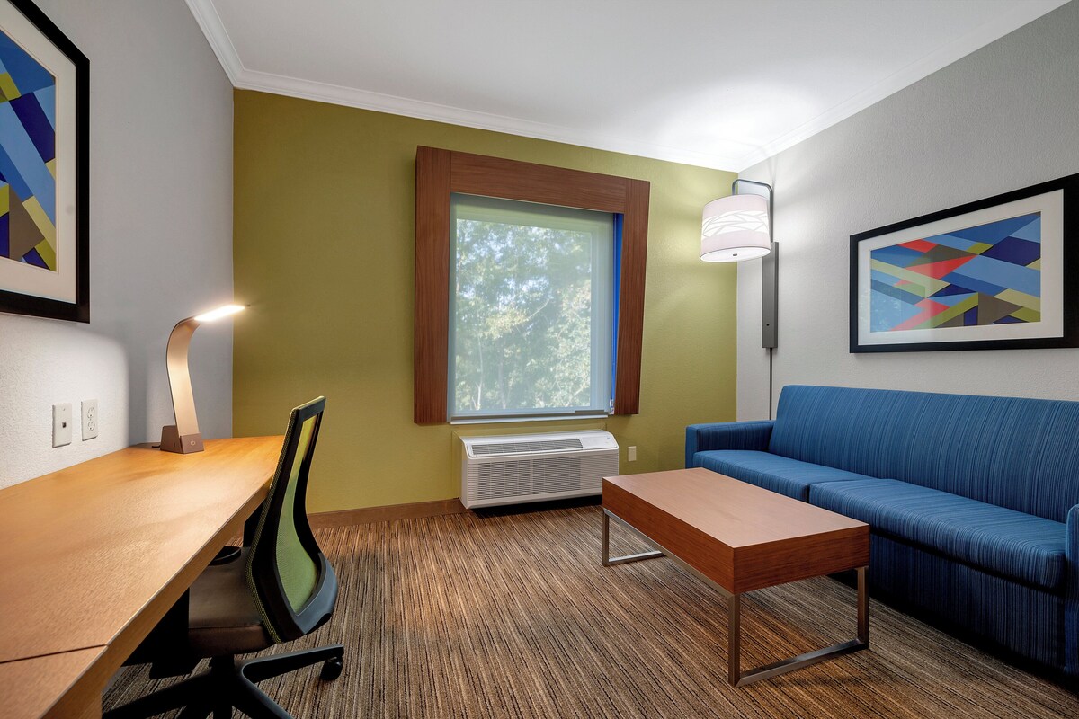 Een hotelkamer met een houten bureau, een blauwe bank, een staande lamp en lijstwerken aan de muur.