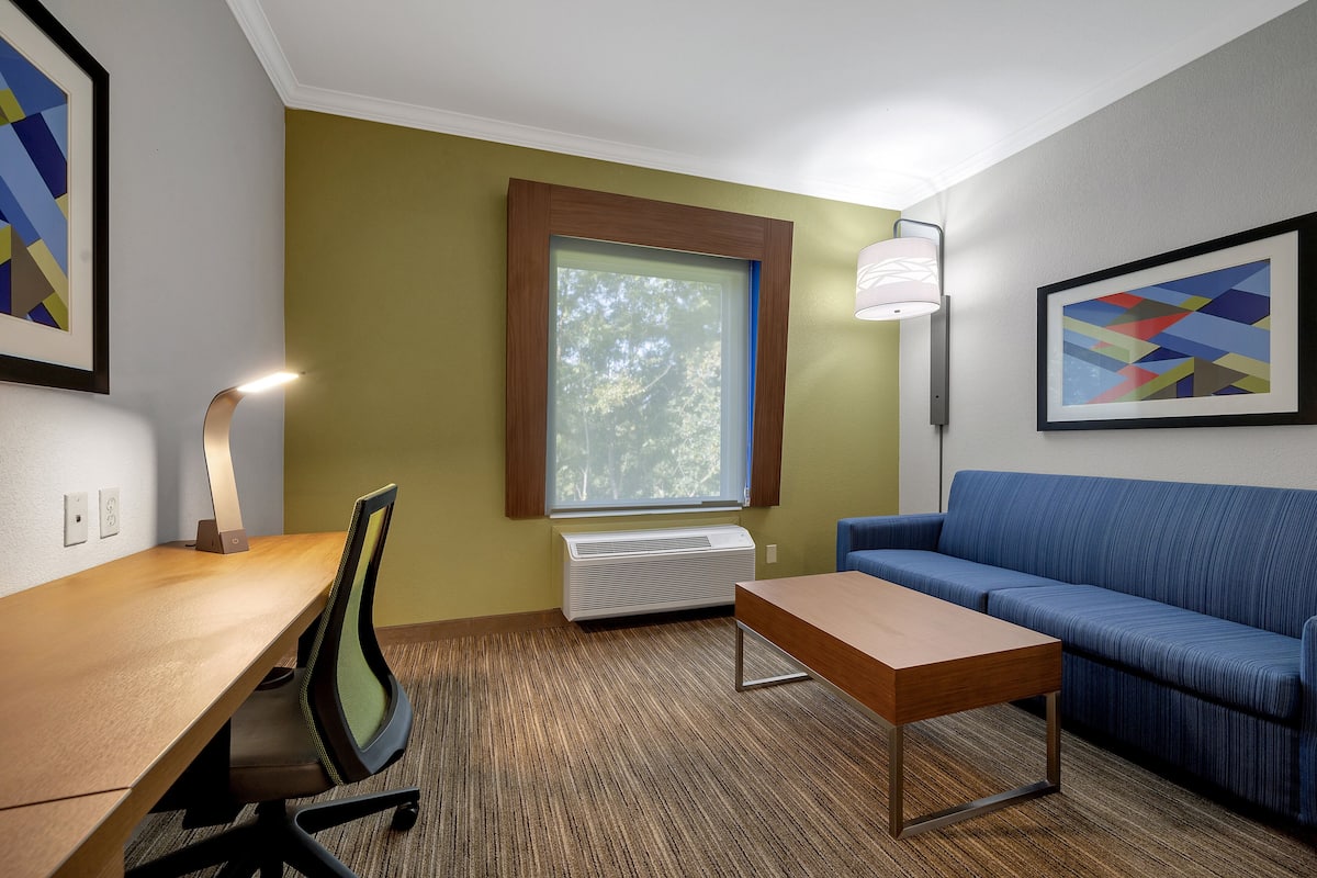 A hotel room with a wooden desk, a blue sofa, a standing lamp, and framed artwork on the walls.