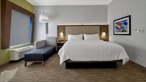 Habitación de hotel con una cama grande, un banco, una lámpara de pared e imagen enmarcada.