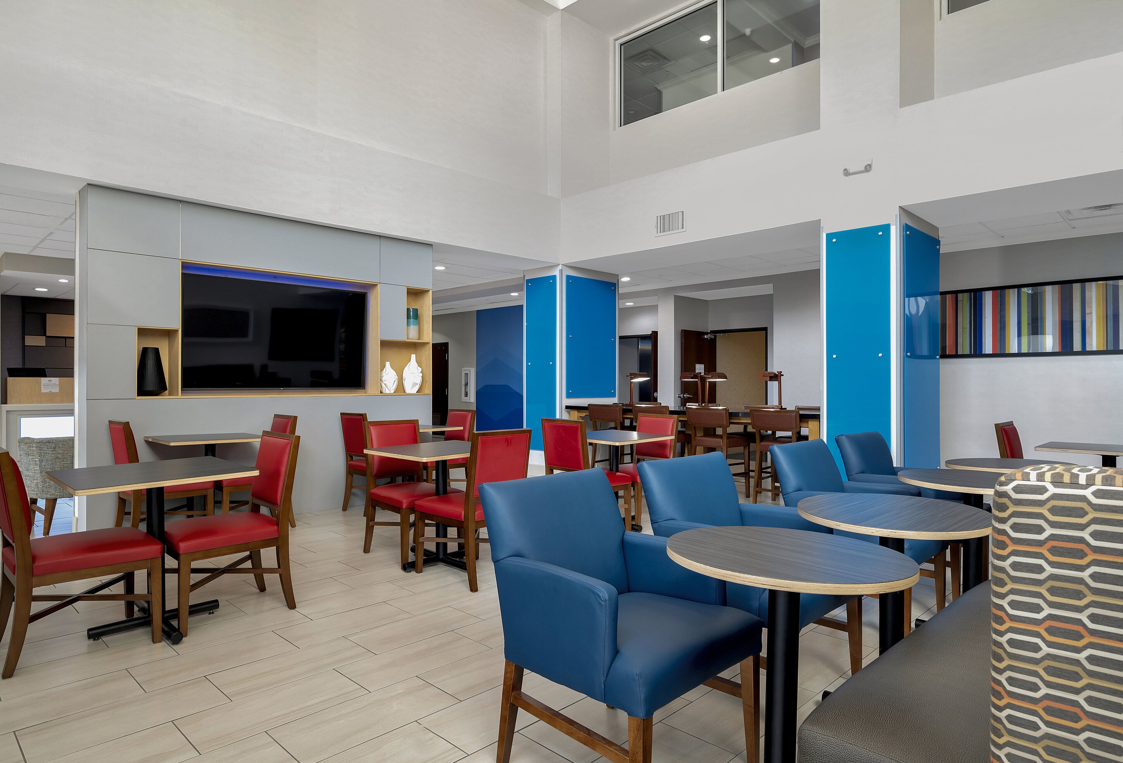 A modern dining area with multiple tables and chairs, a large flat-screen TV, and a blue accent wall.