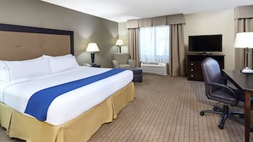 Habitación de hotel con una cama grande, un escritorio, una silla, televisión y ventana con cortinas.