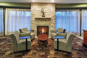 Una habitación con chimenea de piedra, dos sillones, una mesa redonda y alfombra estampada.
