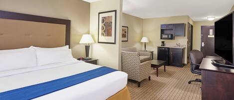 A hotel room with a large bed, a desk, a chair, a television, and a kitchenette.