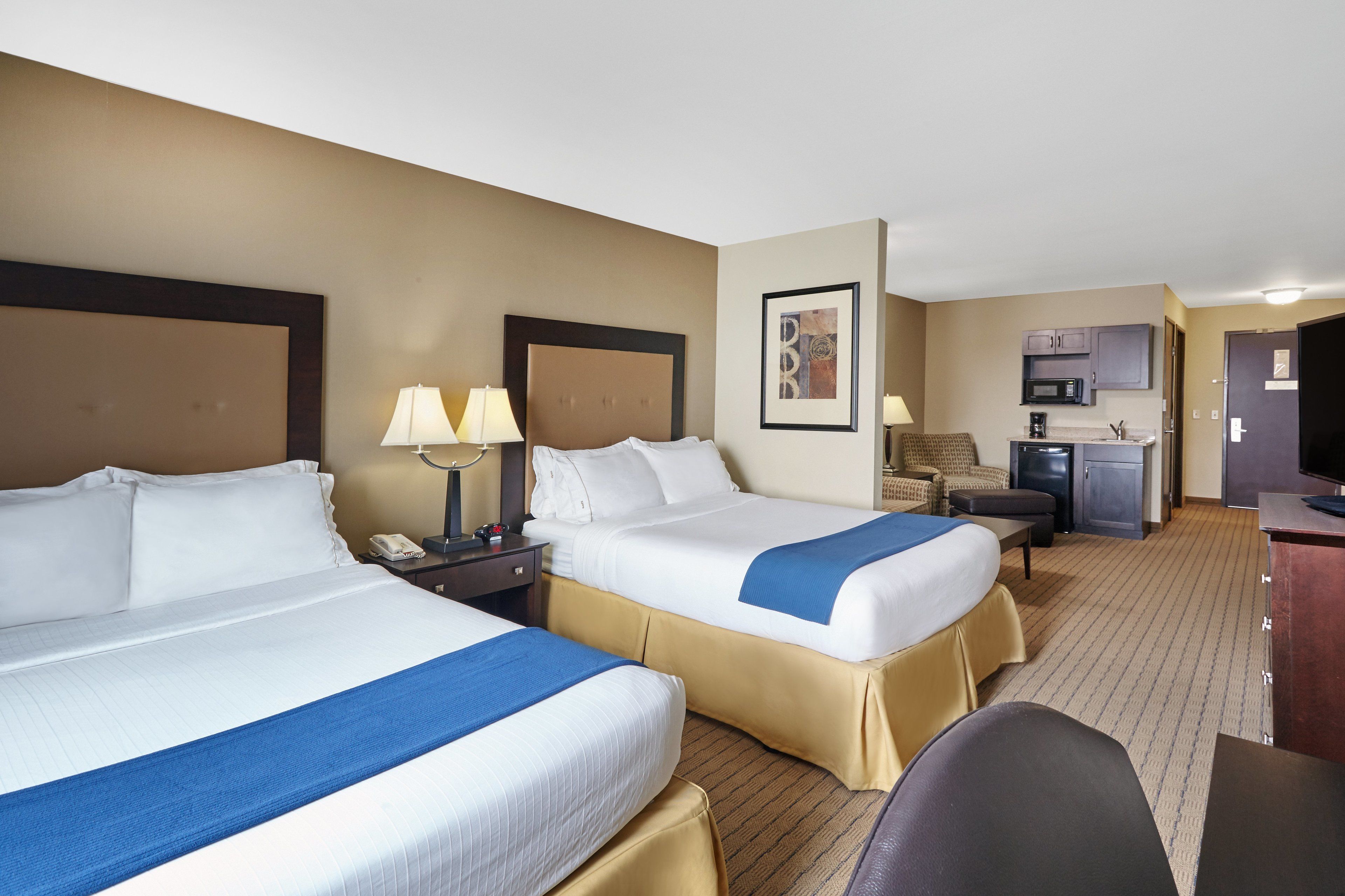 A hotel room with two beds, a desk, a chair, a microwave, and a television.