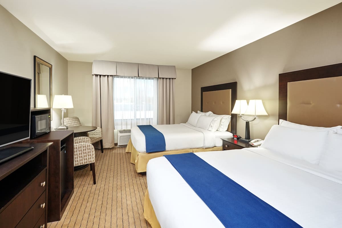 A hotel room with two beds, a TV, a desk, and a chair.