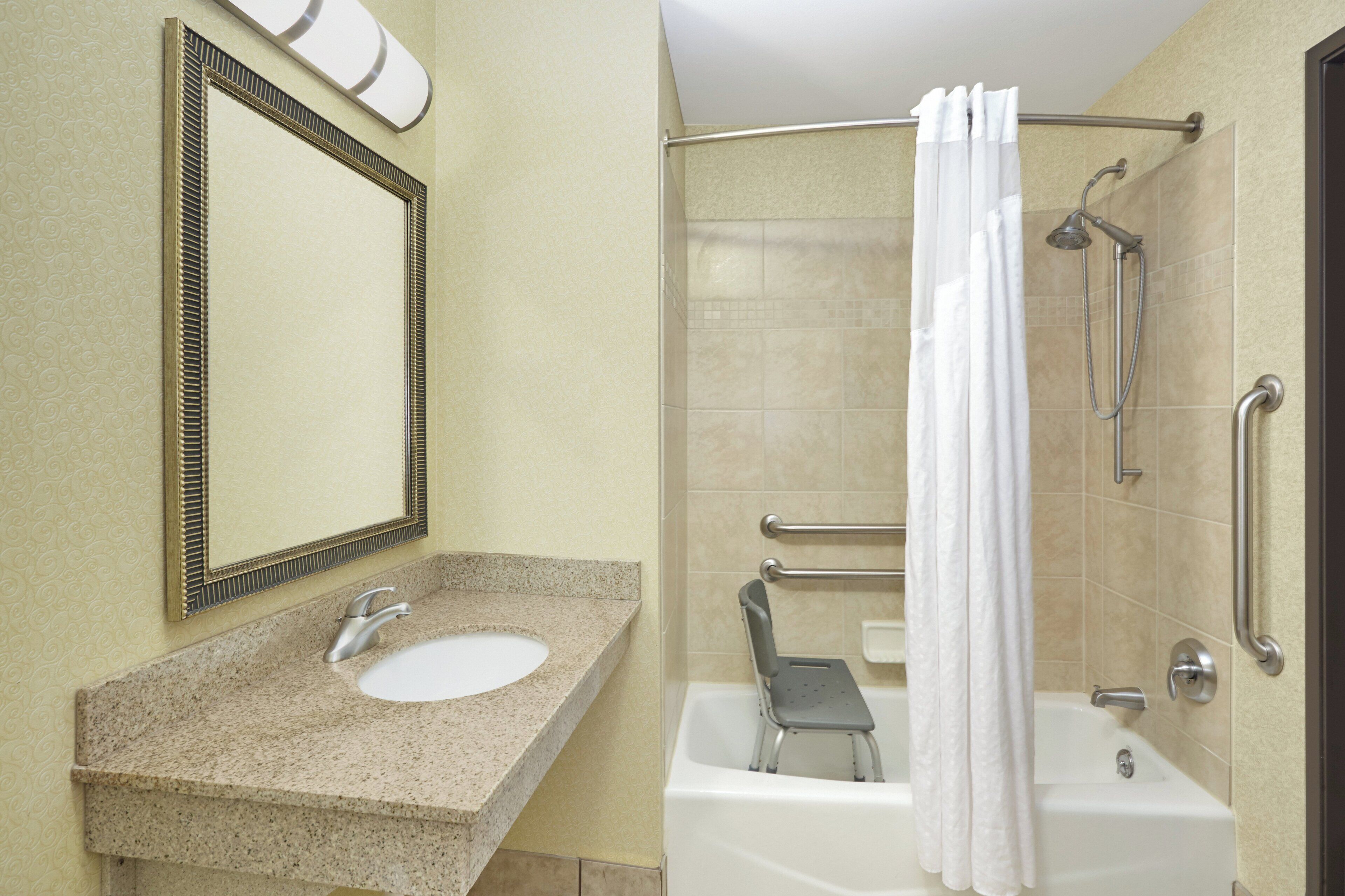 A bathroom with a sink, mirror, shower, and grab bars.