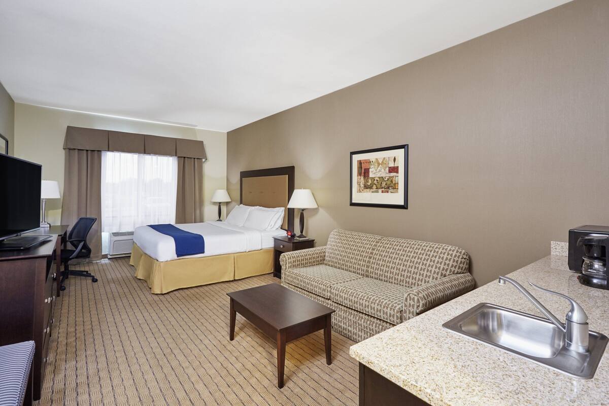A hotel room with a bed, a sofa, a desk with a computer, a coffee maker, and a sink.
