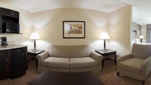 Une chambre d’hôtel équipée d’un canapé, de deux fauteuils, d’une machine à café et d’une œuvre d’art encadrée au mur.