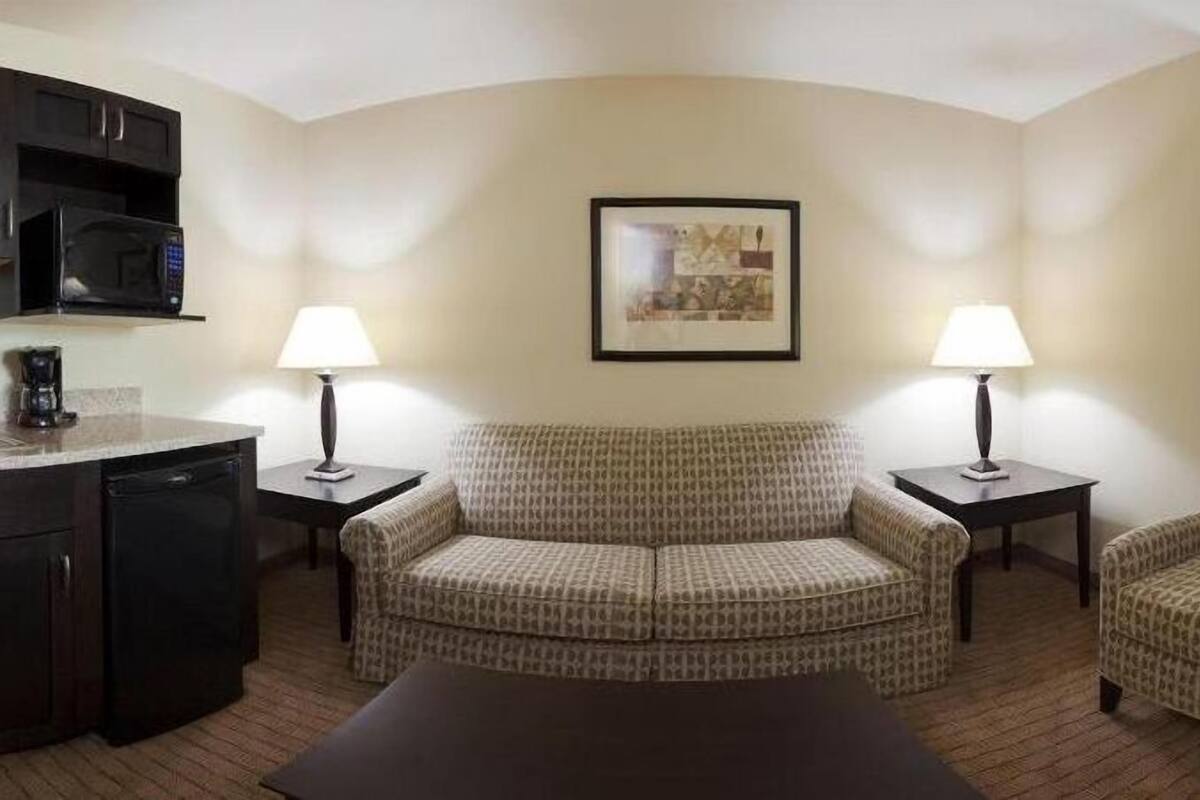 Habitación de hotel con un sofá, dos sillones, una cafetera y una obra de arte enmarcada en la pared.
