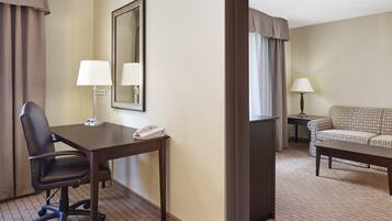 A hotel room with a desk, office chair, two lamps, a sofa, and a mirror.