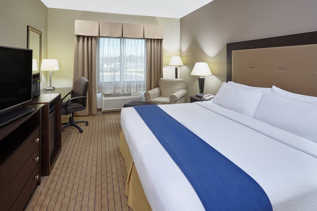 A hotel room with a large bed, a desk with a TV, a chair, and a window with curtains.