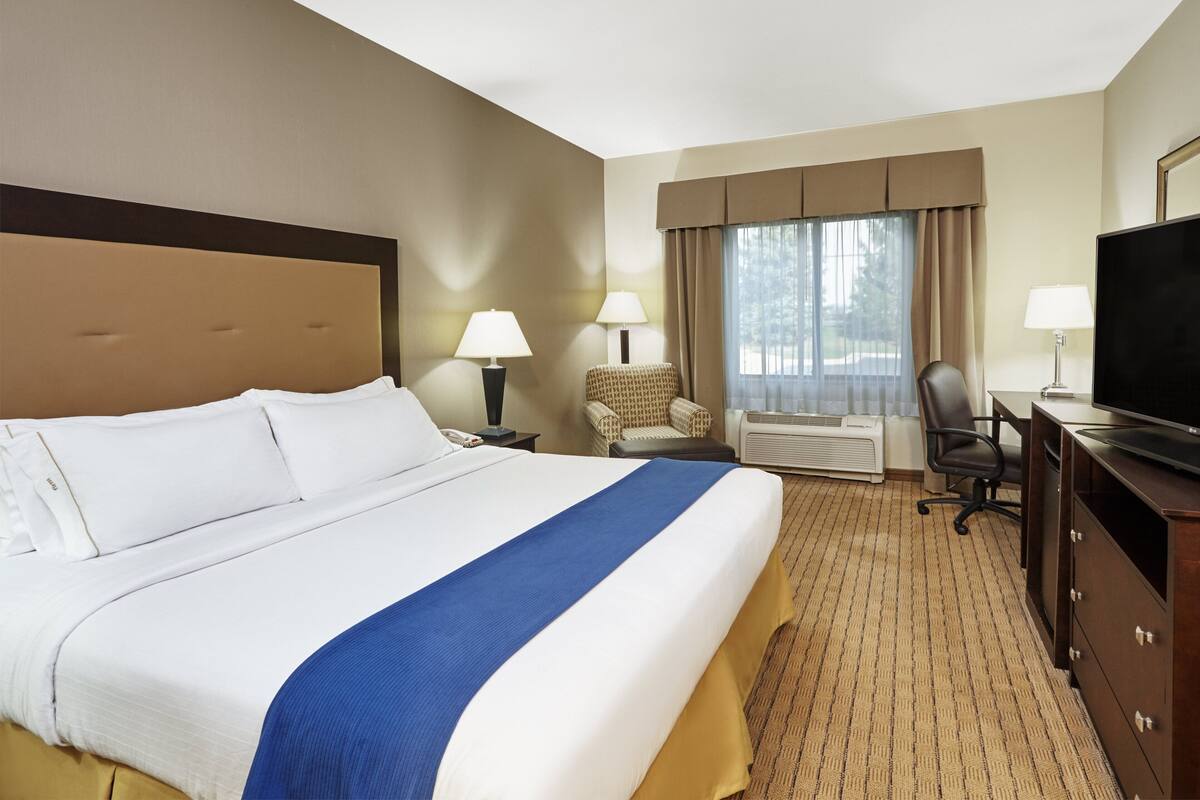 A hotel room with a large bed, two bedside lamps, a television, a desk, and a chair.
