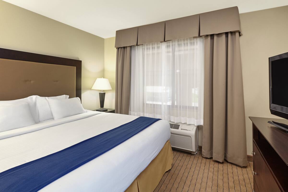 A hotel room with a large bed, a flat-screen TV, a desk, and a window with curtains.