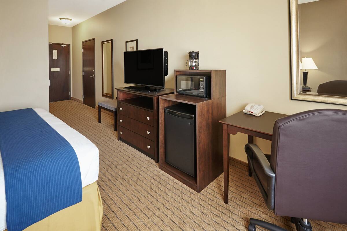 A hotel room with a bed, a desk with a telephone, a microwave, a television, and a coffee maker.