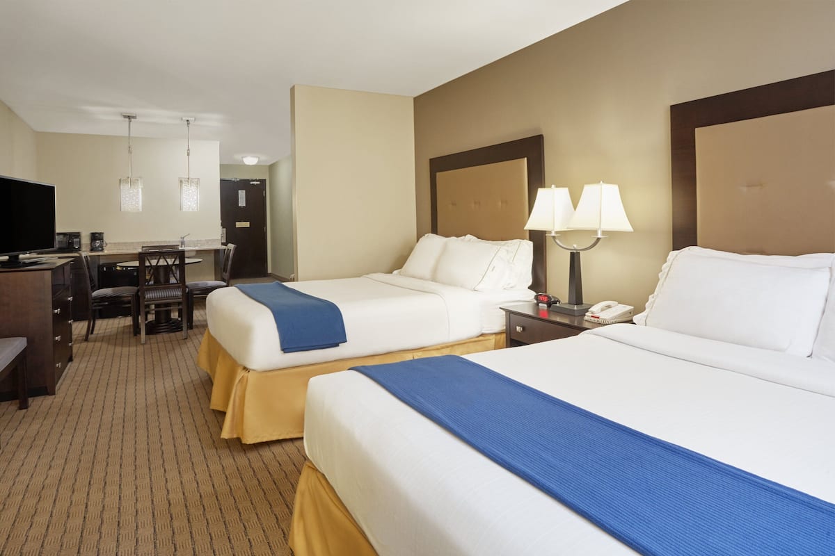 A hotel room with two beds, a desk, a chair, and a television.