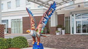 A sculpture of a bird with wings, placed on a concrete base, in front of a building with a brick facade and large windows. - Holiday Inn Statesboro-University Area by IHG (Statesboro)