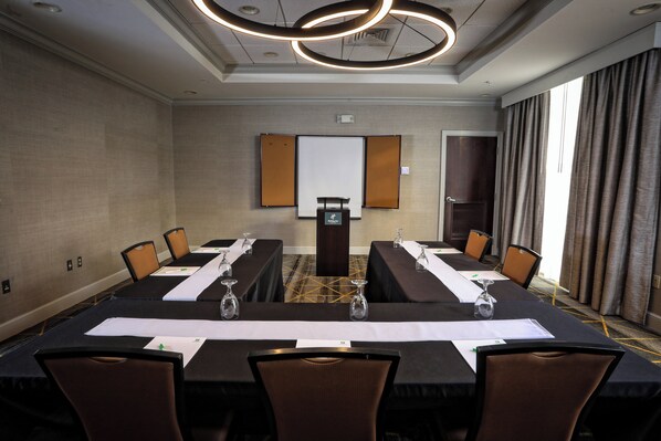 Un salón de conferencias con una larga mesa, sillas, una pantalla de proyector y una puerta.