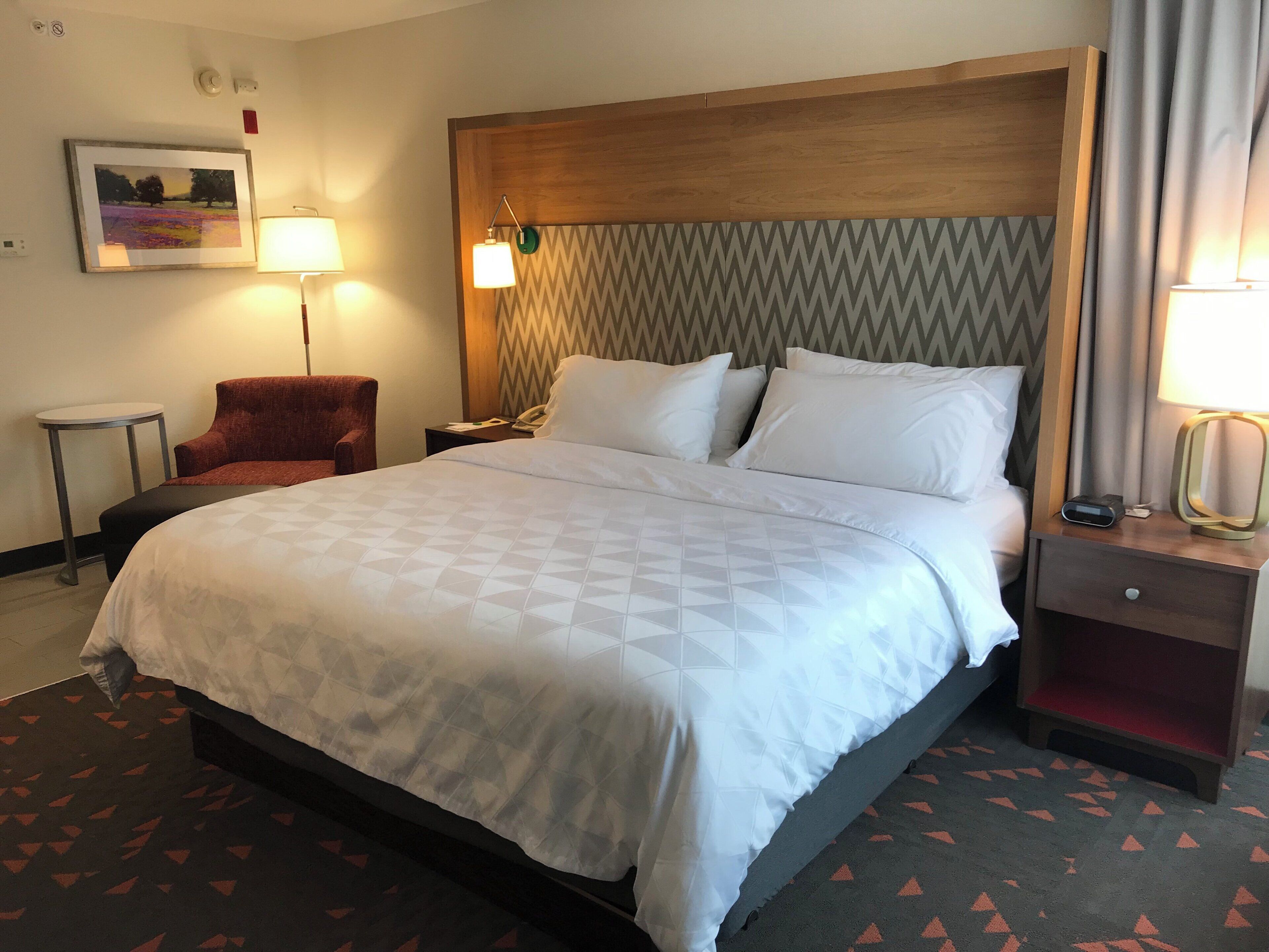 Une chambre d’hôtel avec un grand lit, une chaise, une table de chevet avec une lampe et un téléphone fixé au mur.