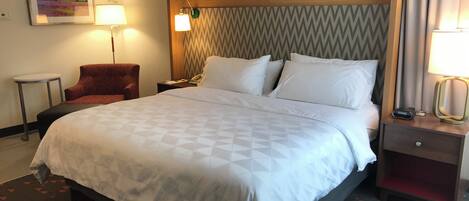 Une chambre d’hôtel avec un grand lit, une chaise, une table de chevet avec une lampe et un téléphone fixé au mur.