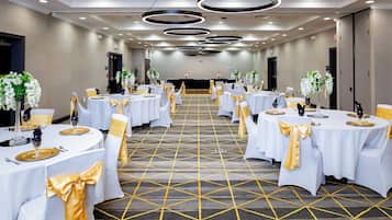 Une salle de banquet d’hôtel avec des tables rondes, des nappes blanches, des rubans dorés et des centres de table floraux.