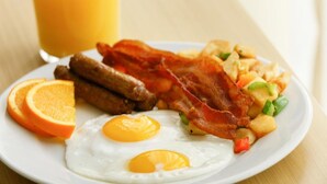 A breakfast plate with eggs, bacon, sausages, and a fruit salad. - Holiday Inn Statesboro-University Area by IHG (Statesboro)