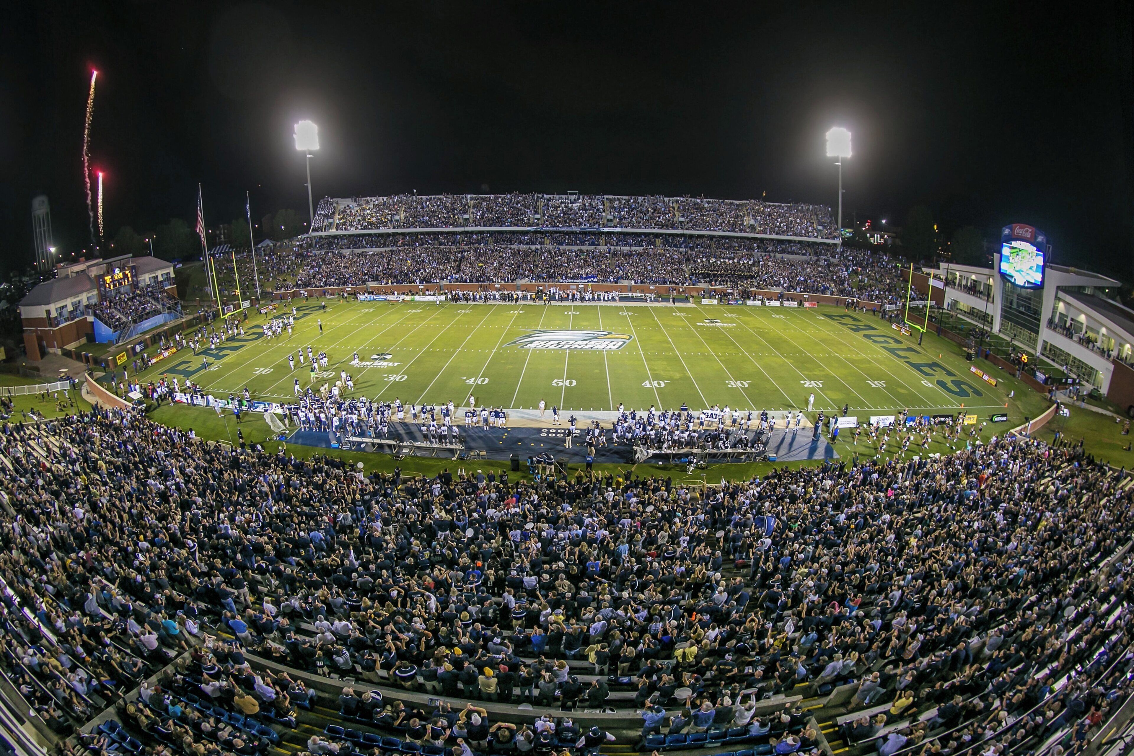 A stadium with multiple tiers of seating, a football field, and a large crowd.