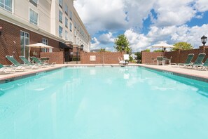 A swimming pool with lounge chairs and umbrellas, surrounded by a brick wall and a building with multiple windows. - Holiday Inn Statesboro-University Area by IHG (Statesboro)