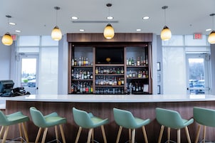 A bar area with a wooden counter, multiple shelves of liquor bottles, and four green bar stools.