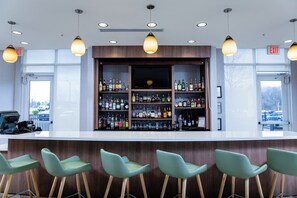 A bar area with a wooden counter, multiple shelves of liquor bottles, and four green bar stools. - Holiday Inn Statesboro-University Area by IHG (Statesboro)