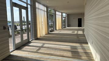 A hallway with large windows, a striped floor, and a fire alarm on the wall.