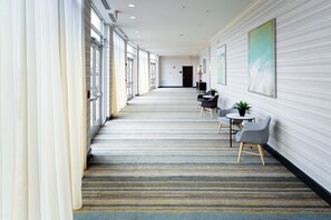 A hotel corridor with a striped carpet, a reception desk, and a seating area with chairs and a table. - Holiday Inn Statesboro-University Area by IHG (Statesboro)