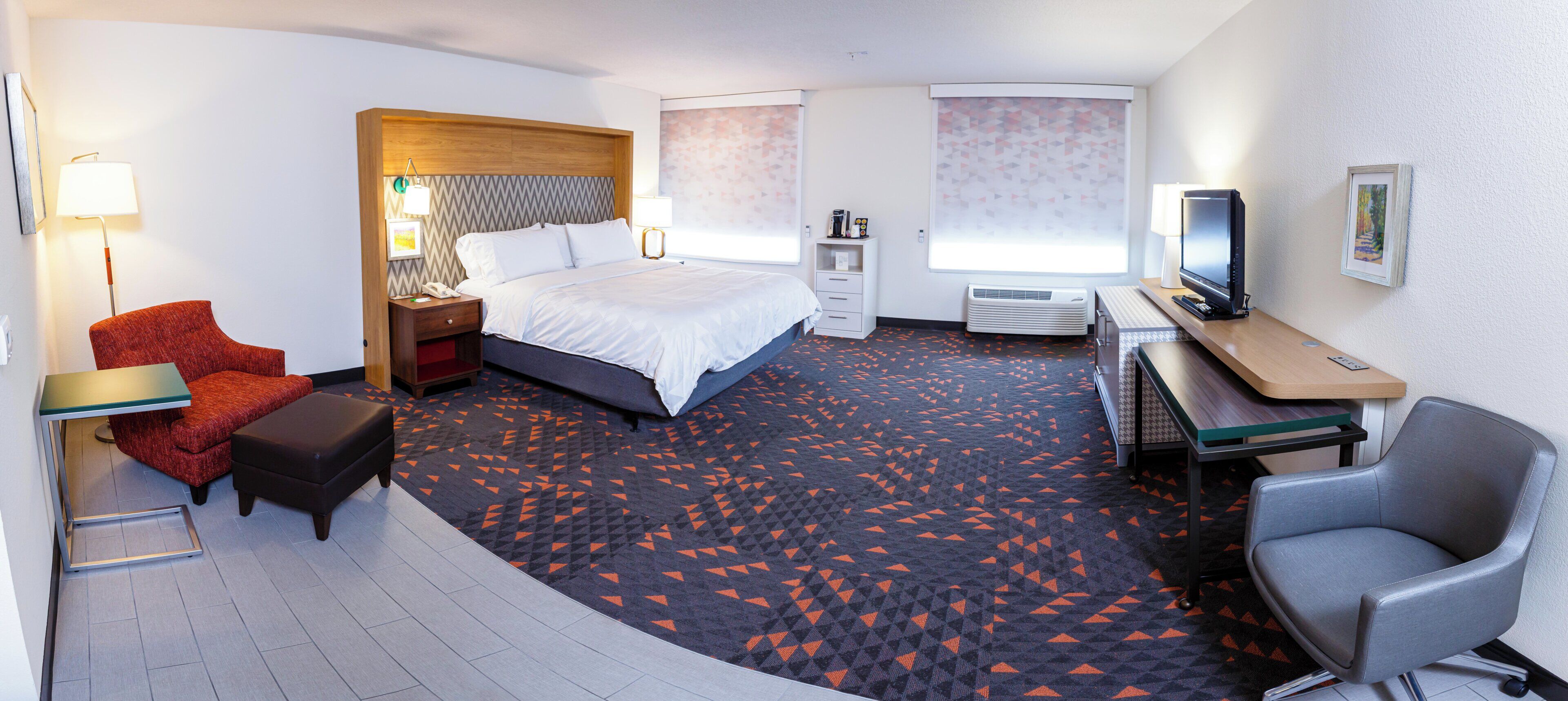 A hotel room with a bed, desk, chair, and a television.