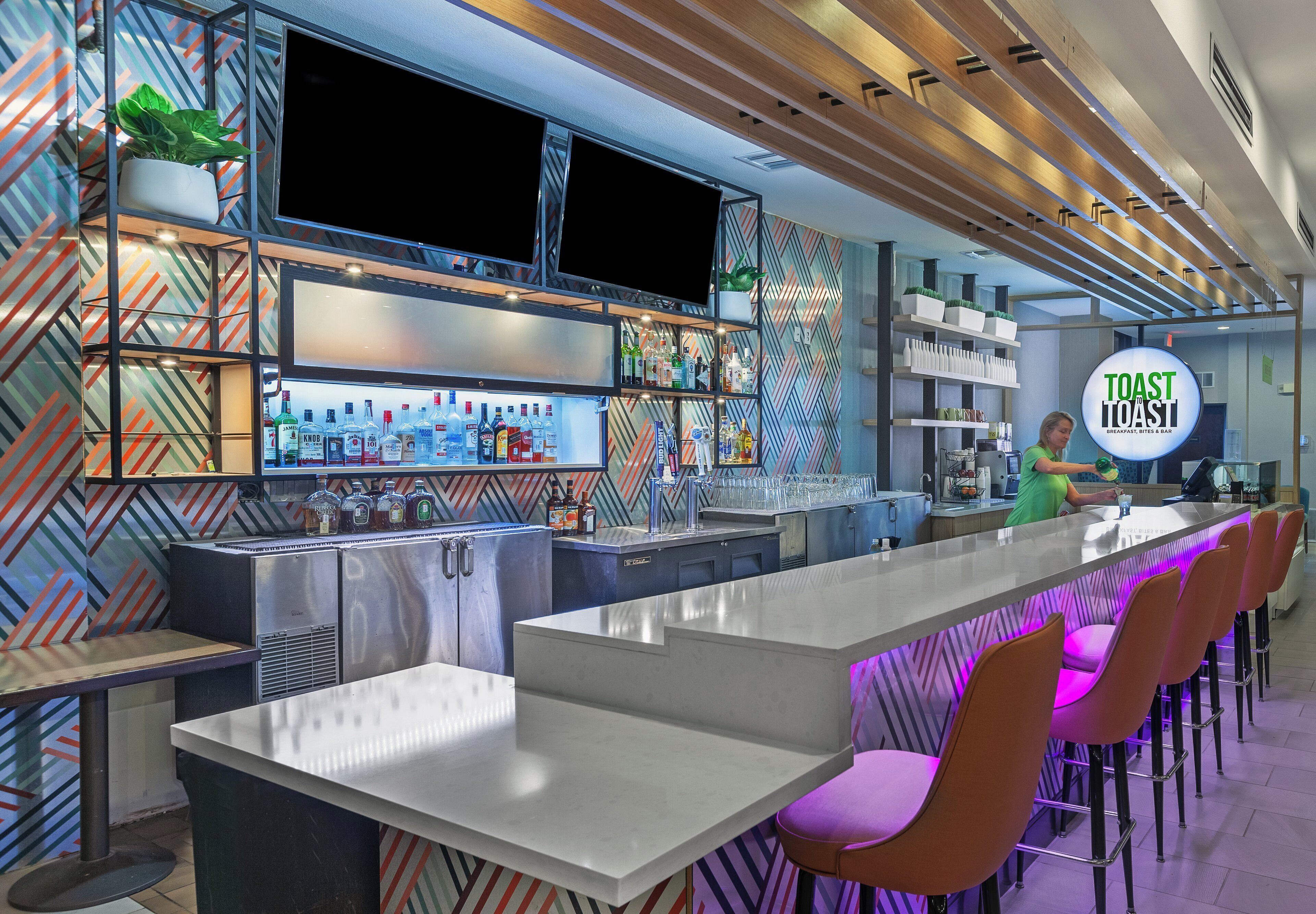 Un área de bar moderna con una barra larga, taburetes y una variedad de botellas de licores.