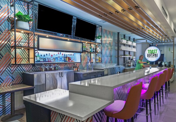 A modern bar area with a long counter, bar stools, and a variety of liquor bottles.