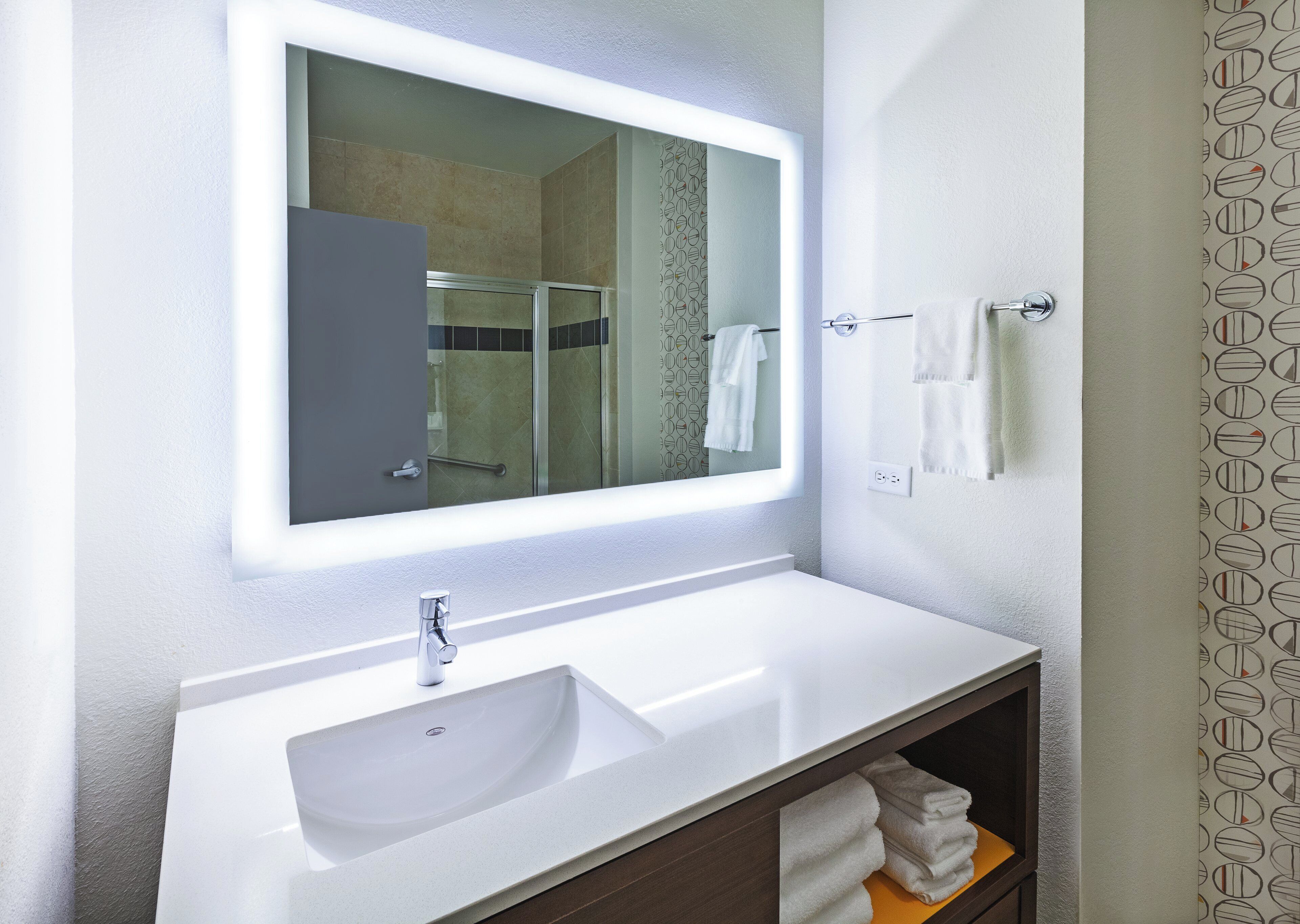 A bathroom with a white sink, a mirror with a light, a towel rack, and a shower area.