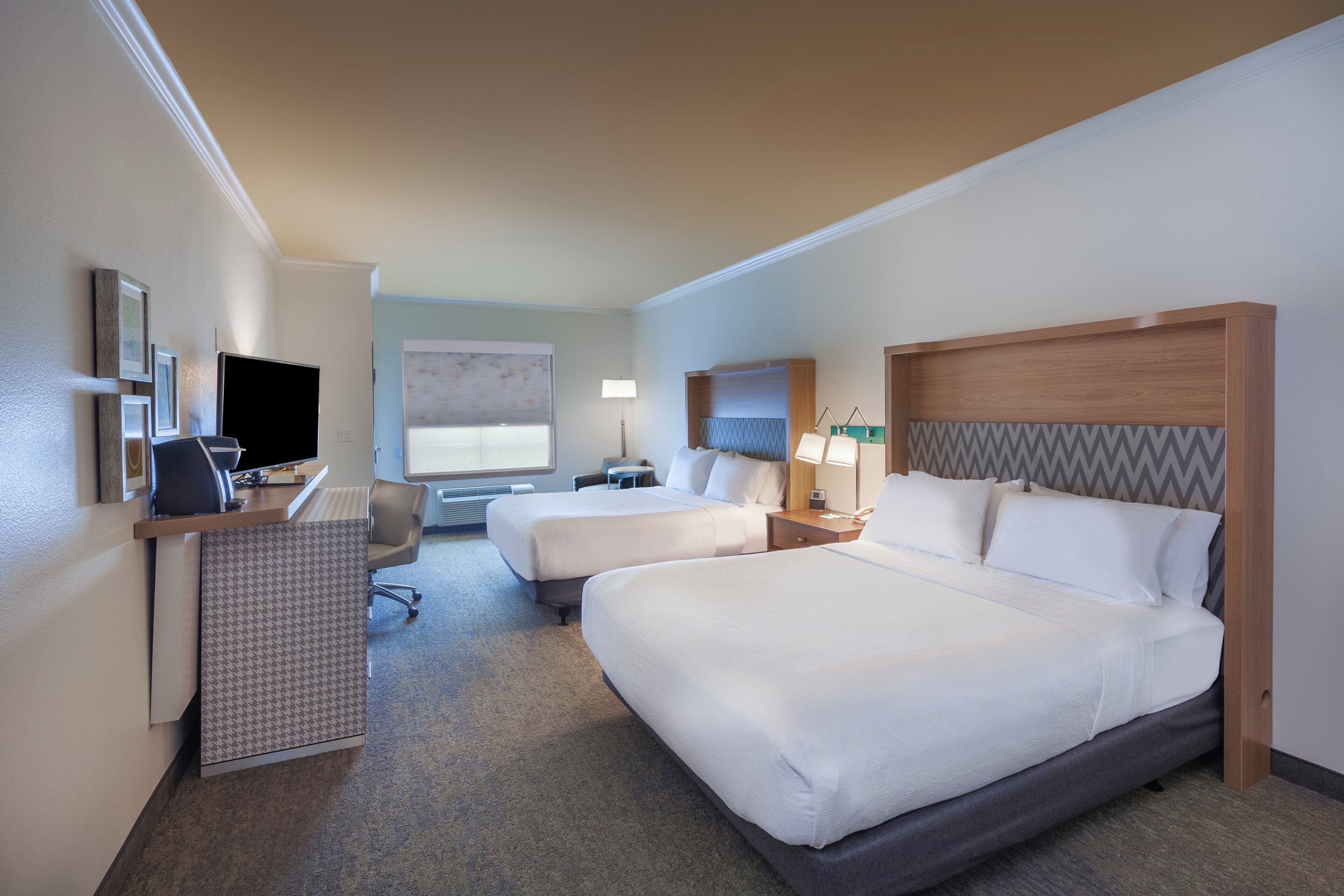 A hotel room with two beds, a desk, a chair, a TV, and a window.