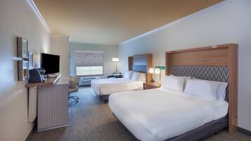 A hotel room with two beds, a desk, a chair, a TV, and a window.