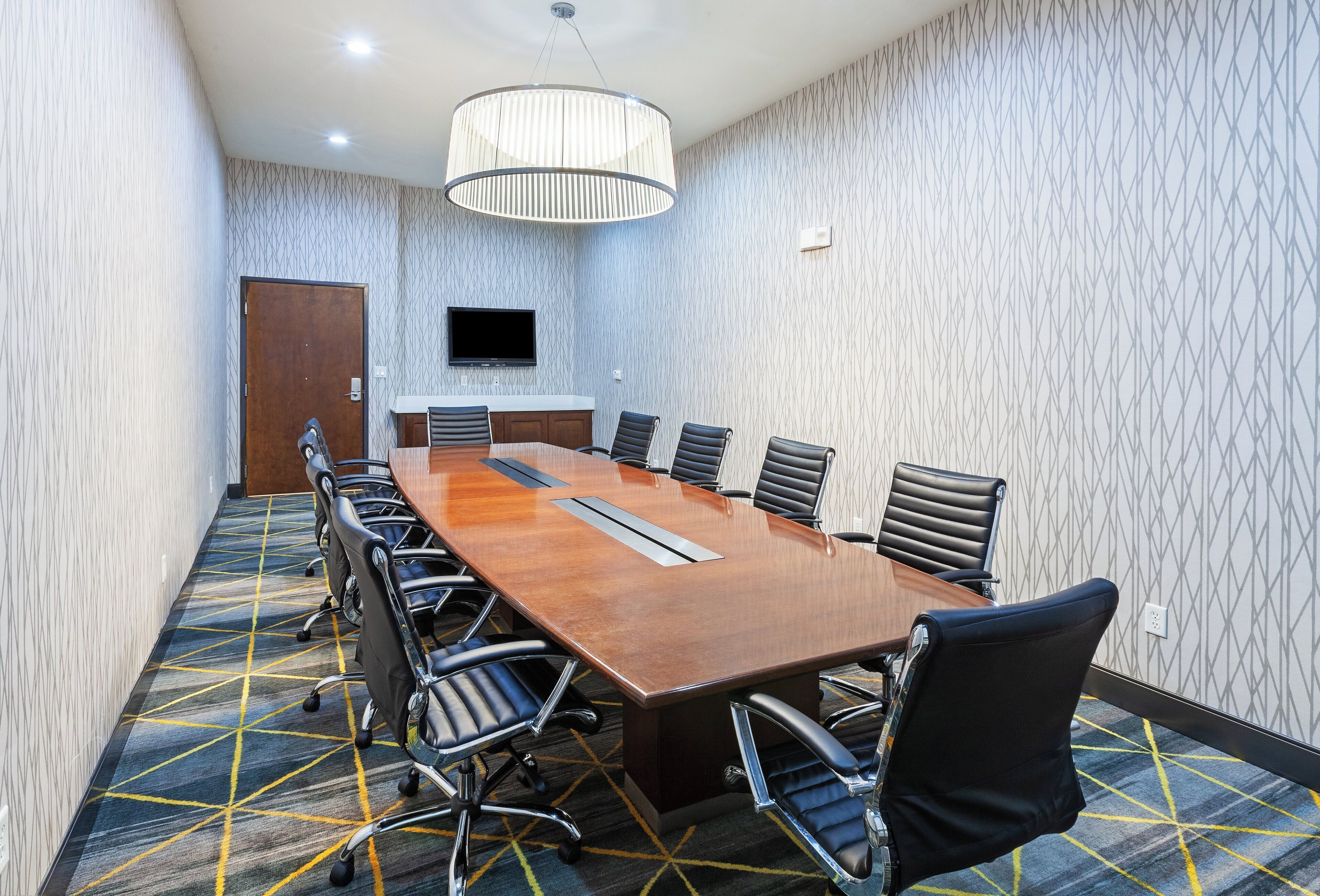 A conference room with a long table, chairs, a television, and patterned carpet.