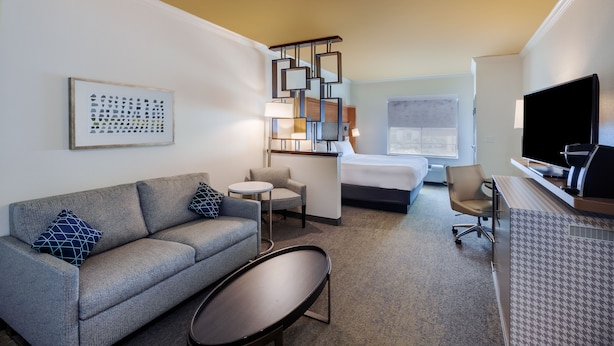 Ein Hotelzimmer mit einer Couch, einem kleinen runden Tisch, einem Bett, einem Schreibtisch mit Computer und einem Fernseher.