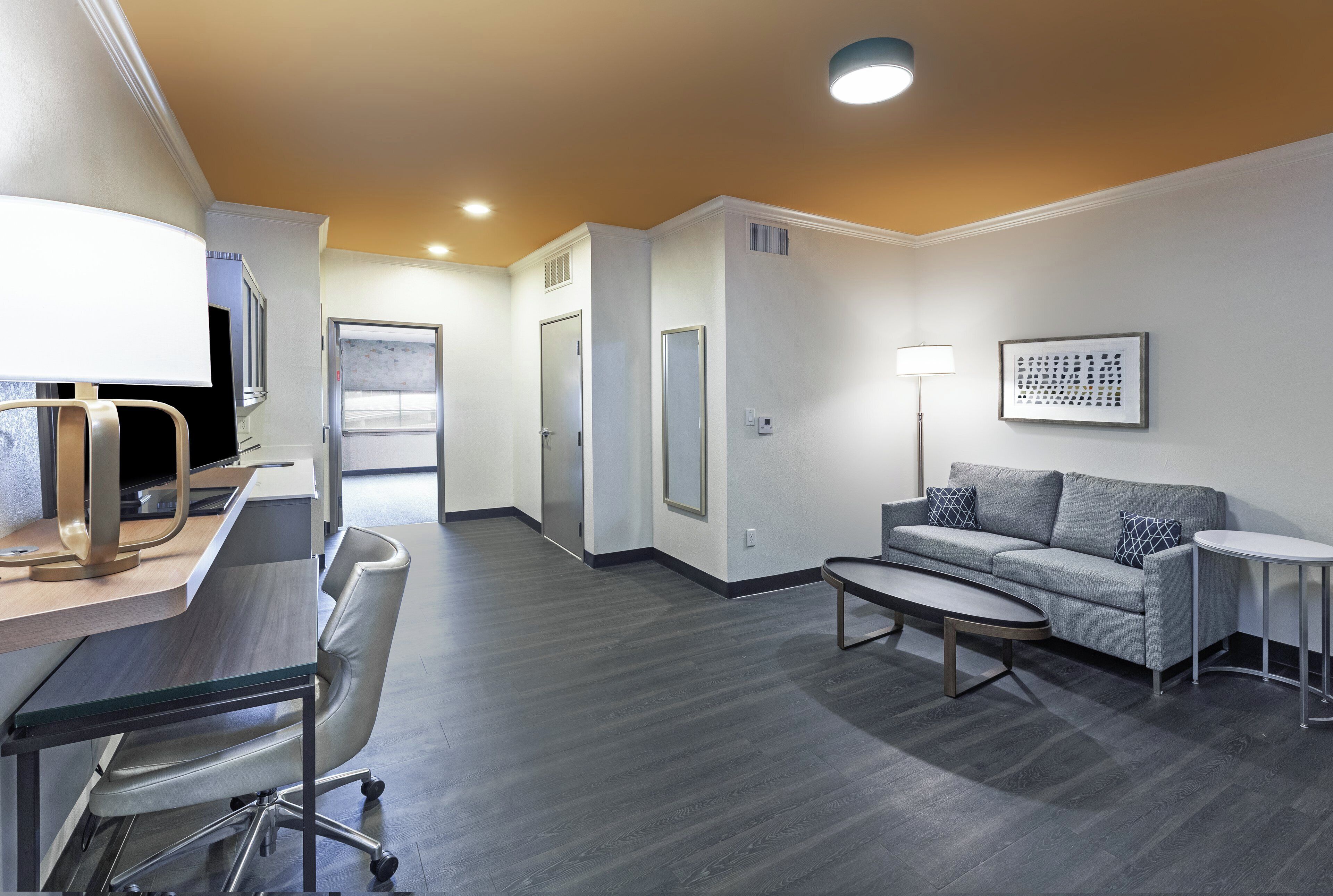 Une chambre d’hôtel moderne équipée d’un bureau, d’un fauteuil de bureau, d’un canapé et d’une petite table.