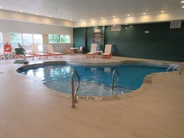 Una piscina interior con agua cristalina, rodeada de sillas de descanso y una pared de azulejos.