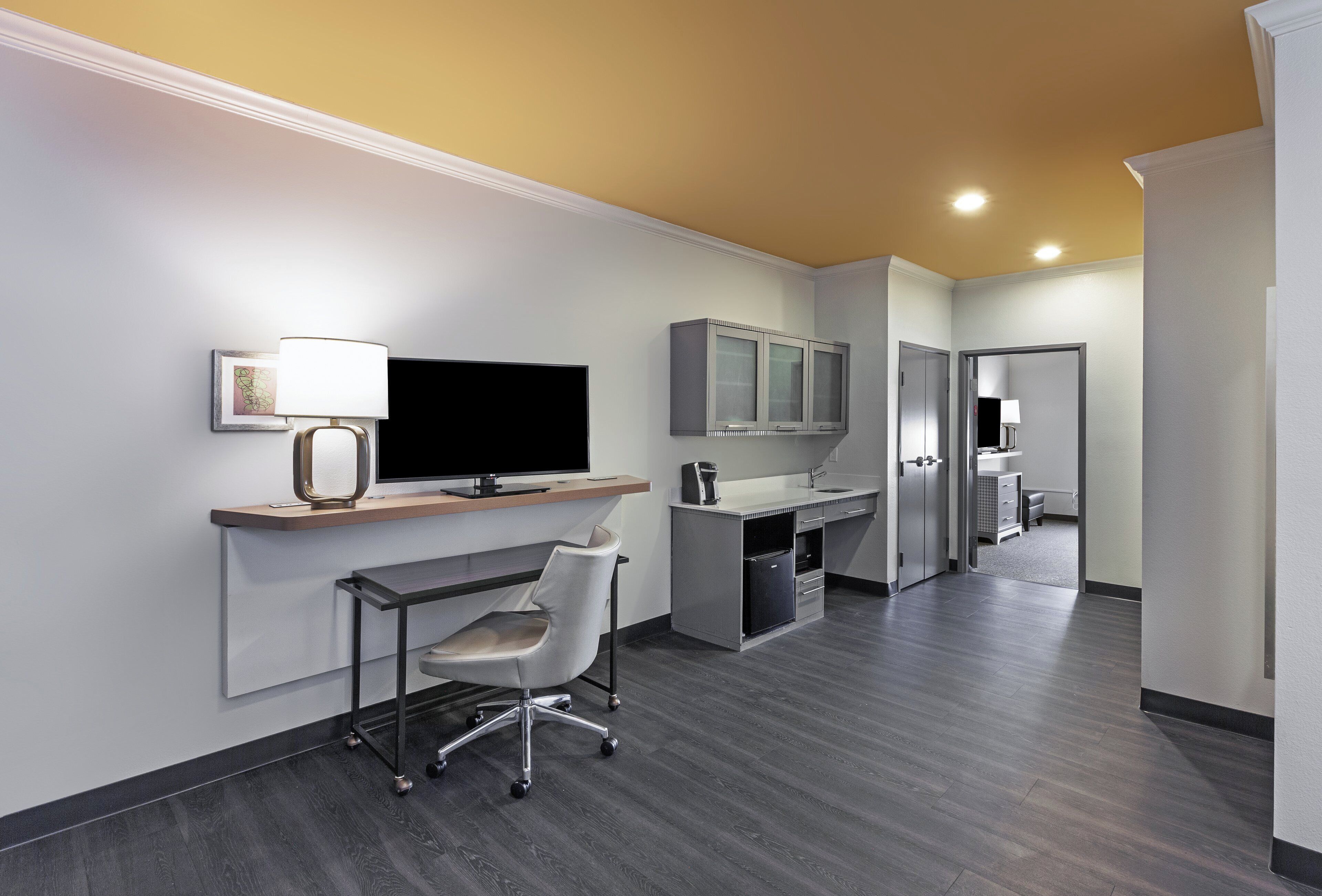 Una habitación de hotel moderna con un televisor de pantalla plana, un escritorio con silla, una kitchenette pequeña y un vestidor.