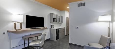 Quarto de hotel compacto com cozinha compacta, TV de tela plana, escrivaninha com cadeira e sofá com almofada.