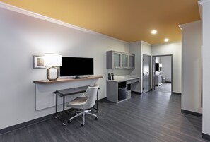 Un espace de bureau moderne comprenant un bureau, une chaise, un téléviseur et des armoires.
